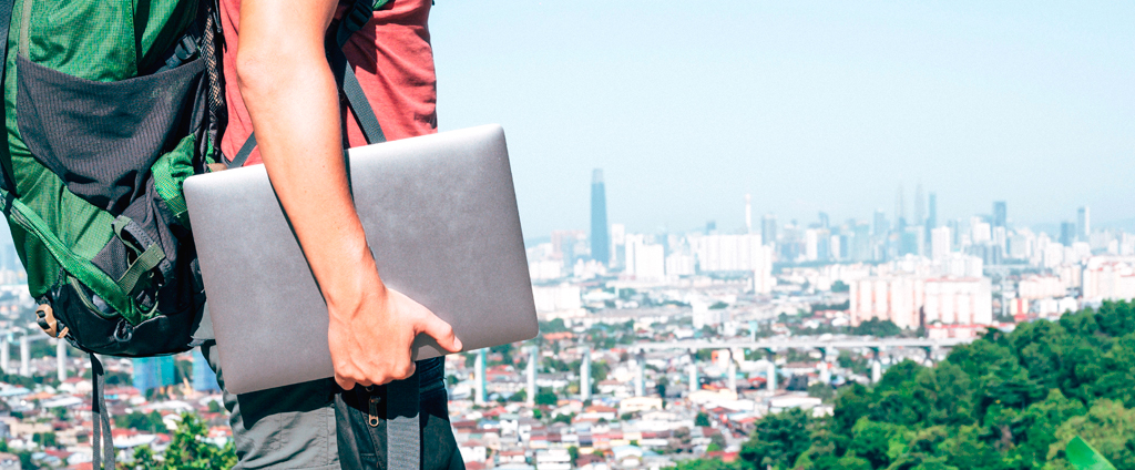 Person with backpack holding a laptop while overlooking a city from a viewpoint